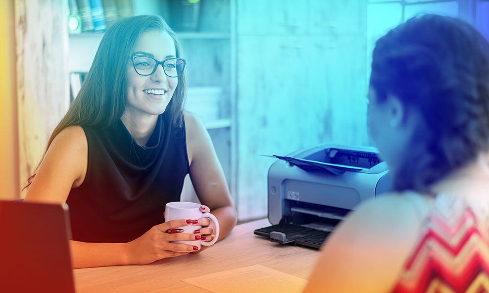 Two women talking over a desk. 